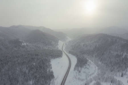 Snowy road runs in the forest in the mountains through the pass in December. A car driving through the winter snowy forest on a country road in the winter.の写真素材