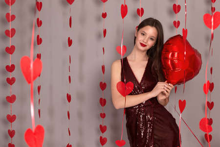 A young girl filming in the studio on a gray background with red heart balloons, the holiday is Valentines Day. Female hands holding red hearts looking into the camera close-up.の写真素材