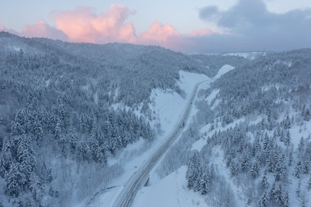 The highway passes through the pass in winter, top view of the snowy forest in winter. Snow-covered road runs through the forest in the mountains through the pass in December.の写真素材