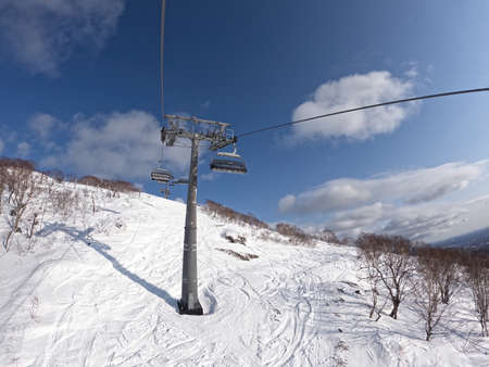 On a sunny winter day in a ski resort, the lift goes up, carries people, top view from a chair lift on a snowy background. A cable car that transports skiers and snowboarders on a winter slope.の写真素材