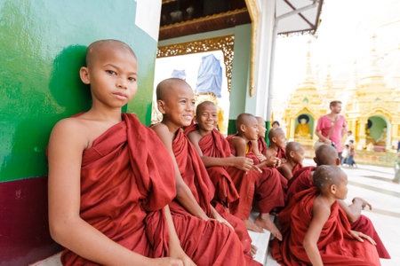OLD BAGAN, MYANMAR- OCT 15, 2013 : Group of unidentified young novice monks sitting down at Shwedagon Pagoda Temple, Myanmar on October 15, 2013. 89% of the Burmese population is Buddhist.のeditorial素材
