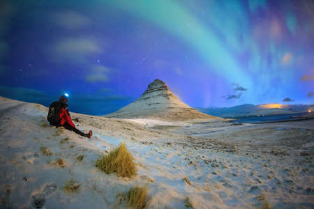 Spectacular northern lights appear over Mount Kirkjufellwith a traveller in Iceland.の写真素材