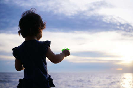 a girl holding a flower while watching the sunset by the beachの写真素材