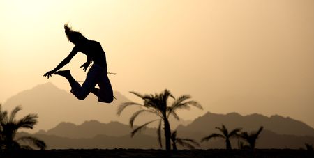 Young woman at sunset jumping up on a mountains and tropical landscape background. 
Excellent image for your banners on summer tourism.の写真素材