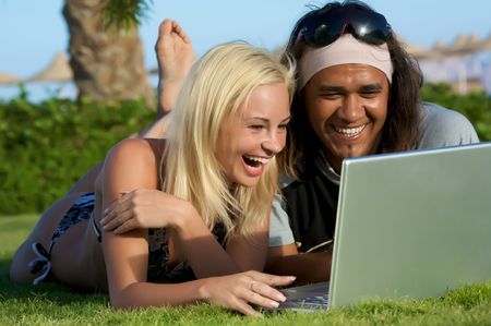 young multi-ethnic couple lay on grass with laptop.の写真素材