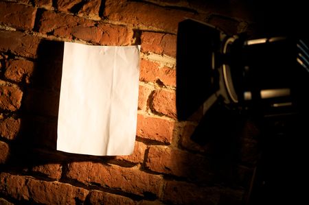 A view of a bright spotlight shining directly on a blank poster or sign on a brick wall at night.の写真素材