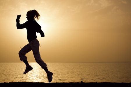 Young woman running on a sunset beach backgroundの写真素材