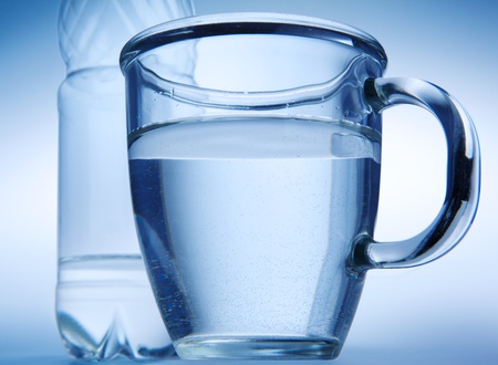 Clear water into a glass mug and  bottle on blue background.の写真素材