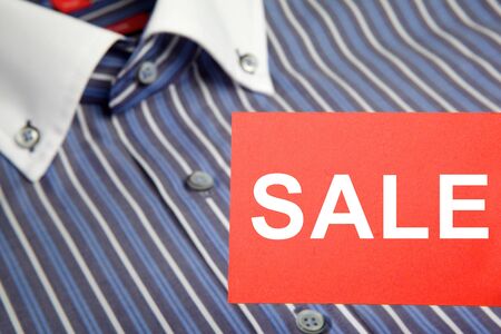 Red label with text SALE in the foreground and blue business men's shirt on background. Focus on foreground. See photo "Labels for retail" in my portfolio for other text label for this image.の写真素材