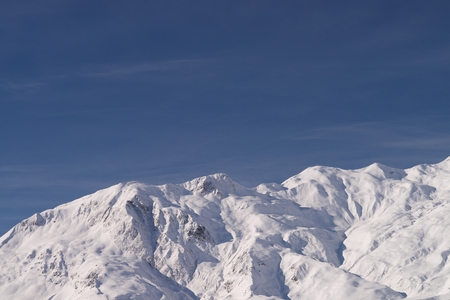 Low sun in Winter on snow covered mountain range with deep crevasses and gulleys, dark blue sky background.の写真素材