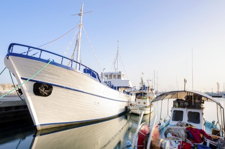 Fishing boats docked at the Limassol old port in Cyprus, next to the Marina part of the ports authority. A view of the harbor, the mediterranean sea, the water, boat and fish nets and fishing equipment.の写真素材