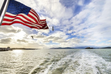 View of San Francisco Bay, the Golden Gate bridge, seagulls flying, the american flag waving and Alcatraz island at sunset from a ferry in California, United States.の写真素材