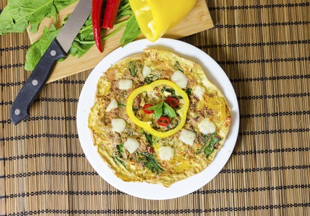 Top view of a spinach, chili, mint and pepper omelette in a dish over bamboo table cloth and chopping board with knife and raw vegetables. A healthy diet meal omelet.の写真素材
