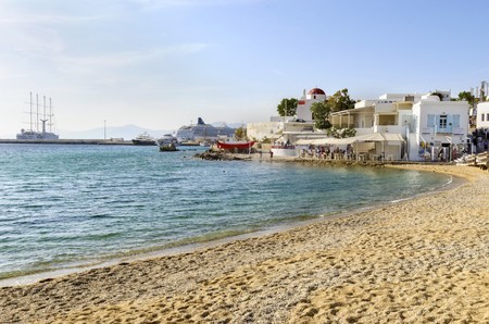 The coastline of Chora in Mykonos, Greece. Typical greek island whitewashed houses on the shore and seaview golden sand promenade overlooking the Aegean sea and calm clean blue water.の写真素材