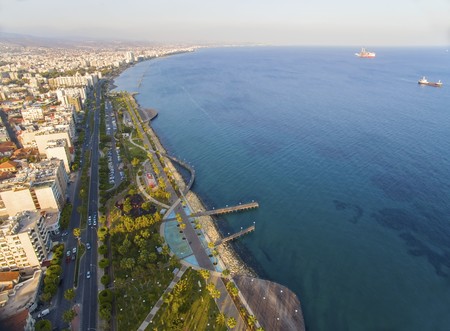 Aerial view of Molos Promenade on the coast of Limassol city in Cyprus. A view of the walk path surrounded by palm trees, pools of water, grass, the Mediterranean sea, piers, rocks and urban skyline.の写真素材