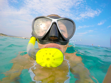 Portrait of a yound woman floating and wearing snorkeling gear in the clean blue sea of Protaras, Cyprus. Close up view of tube, mask, bikini of free diver overthe surface of the water.の写真素材