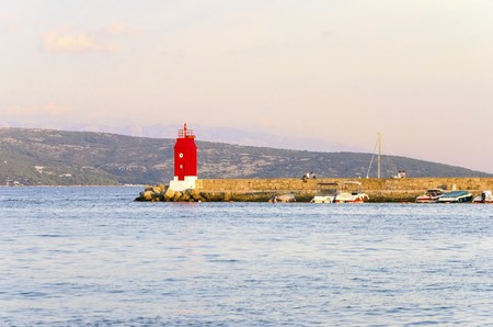The red lighthouse, mole at Krk town, Croatia and boats docked at the harbour pier at sunset. A small cylindrical tower at the biggest port of the island.の写真素材