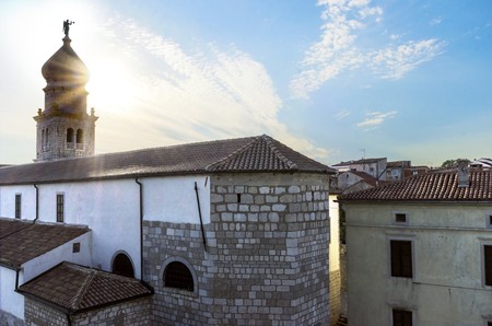 Bell tower of the cathedral, the Church of the Assumption of Blessed Virgin Mary, in Krk, Croatia, a monument of Romanesque era St. Quirinus and Barbara, with a Venetian sculpture of an angel holding a trumpet on top.の写真素材