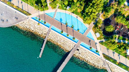 Aerial view of Molos Promenade park on the coast of Limassol city centre in Cyprus. Bird's eye view of the jetties, beachfront walk path, palm trees, Mediterranean sea, piers, rocks, urban skyline and port from above.のeditorial素材
