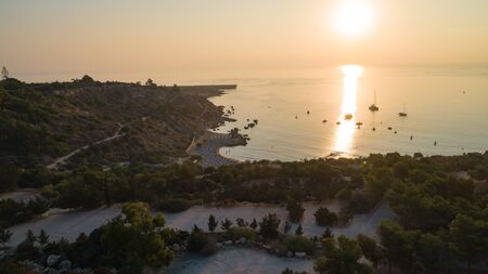 Aerial bird's eye view of Konnos beach in Cavo Greco Protaras, Paralimni, Famagusta, Cyprus. The famous tourist attraction golden sandy Konos bay with boats, sunbeds, water sports, people swimming in sea on summer holidays, at sunrise from above.の写真素材