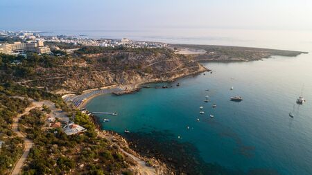 Aerial bird's eye view of Konnos beach in Cavo Greco Protaras, Paralimni, Famagusta, Cyprus. The famous tourist attraction golden sandy Konos bay with boats, yachts, sunbeds, water sports, people swimming in sea on summer holidays, from above.の写真素材
