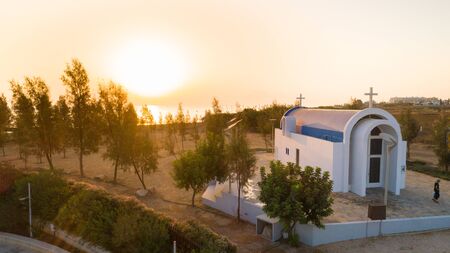 Aerial view of sunset and landmark white washed modern arch chapel of Agia Triada, Protaras, Famagusta, Cyprus from above. Bird's eye view of tourist attraction Ayia Trias blue bay church, by the beach at sunrise in Ammochostos district.の写真素材