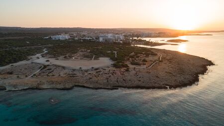 Aerial bird's eye view of Landa beach, Ayia Napa, Famagusta, Cyprus. The landmark tourist attraction golden sand bay at sunrise with sunbeds, sea restaurants between Makronissos and nissi in Agia Napa on summer holidays, from above.の写真素材