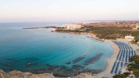 Aerial bird's eye view of Landa beach, Ayia Napa, Famagusta, Cyprus. The landmark tourist attraction golden sand bay at sunrise with sunbeds, sea restaurants between Makronissos and nissi in Agia Napa on summer holidays, from above.の写真素材