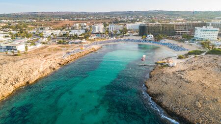 Aerial bird's eye view of Vathia Gonia beach, Ayia Napa, Famagusta, Cyprus. The landmark tourist attraction rocky bay at sunrise with golden sand, sunbeds, sea restaurants in Agia Napa on summer holidays, from above.の写真素材