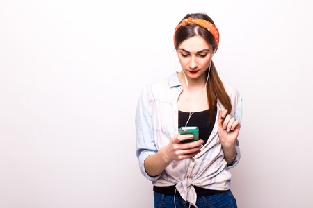 Pretty smiling girl listening the music wearing headphones holding in hand the phone  on white backgroundの写真素材