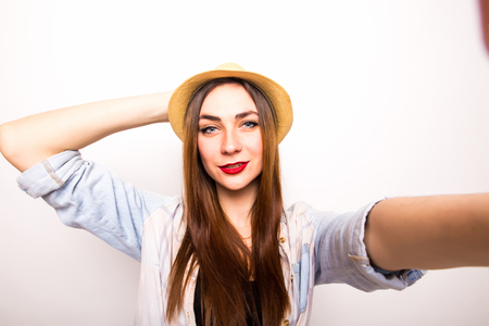 Beautiful stylish girl in hat making selfie on white backgroundの写真素材