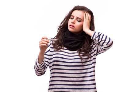 Young sick woman in scarf and home clothes looking at thermometer. Sick girl with a thermometer on a white background, isolate, flu, coldsの写真素材