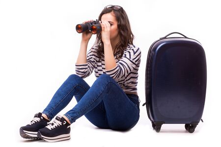 Smart nice girl look over Binoculars, sitting with her big luggage bag on whiteの写真素材