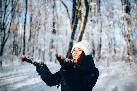 Girl Wearing Warm Winter Clothes And Hat Blowing Snow outdors in the forest catch snowflakesの写真素材