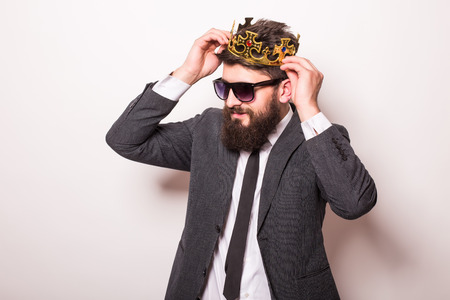 Portrait handsome young cheerful man in suit with crown looking at camera with smile while standing against white backgroundの写真素材