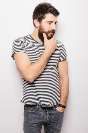 Portrait handsome young man with  hand on beard smiling while standing against white backgroundの写真素材
