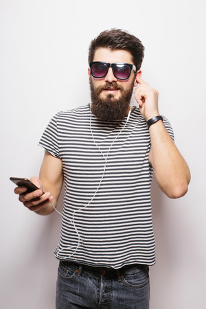 Happy Hipster with beard wearing  shirt and sunglasses enjoying music against white backgroundの写真素材