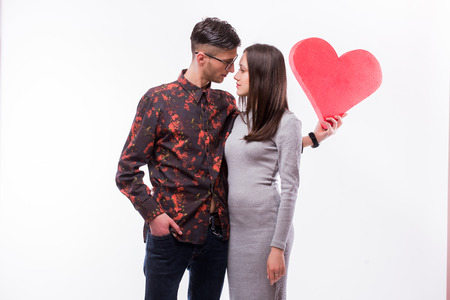 Cool young hipster couple hugging and  holding red heart on white backgroundの写真素材