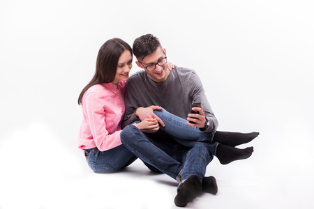 Young hipster man in glasses and woman sitting down and look at phone isolated on the blank white backgroundの写真素材