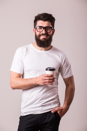 Bearded young man with coffee cup and smiling while standing against grey backgroundの写真素材