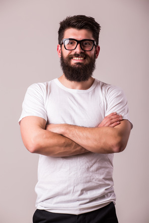 Bearded man in glasses with crossed hands look at camera on whiteの写真素材