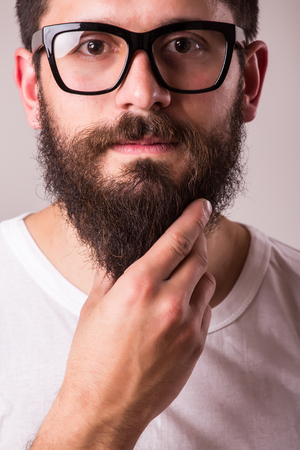 Face portrait of bearded man in glasses with hand on beard against white backgroundの写真素材
