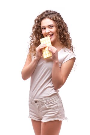 Curly girl eating white chocolate on white backgroundの写真素材