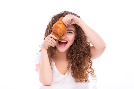 attractive smiling young woman eating croissant for breakfast at table on white backgroundの写真素材