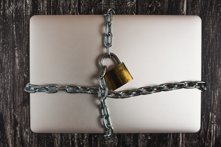 Heavy with a padlock around a laptop isolated on grey table.の写真素材