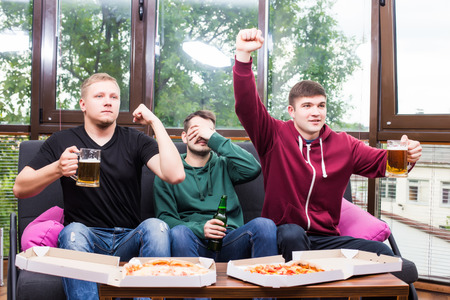 Young friends cheering and drinking alcohol while watching soccer match at homeの写真素材