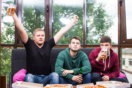 Young friends cheering and drinking alcohol while watching soccer match at homeの写真素材