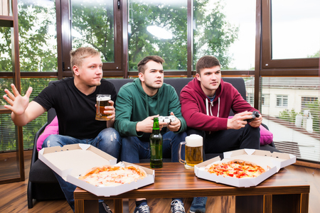 friendship, technology, games and home concept - smiling male friends playing video games, drink beer and have fun at homeの写真素材