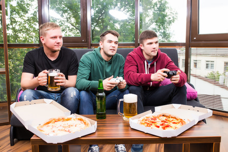 friendship, technology, games and home concept - smiling male friends playing video games, drink beer and have fun at homeの写真素材