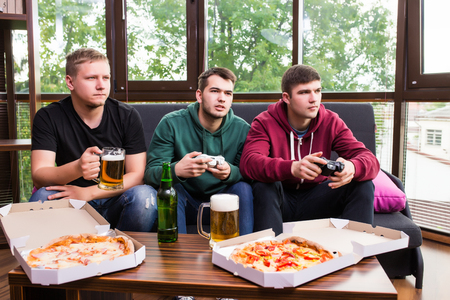 Young men drink beer, eat pizza and play video games  at homeの写真素材